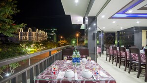 A restaurant with tables set for dining, outdoor seating, and a view of a cityscape at night. - Hong Chau Hotel (Da Nang)