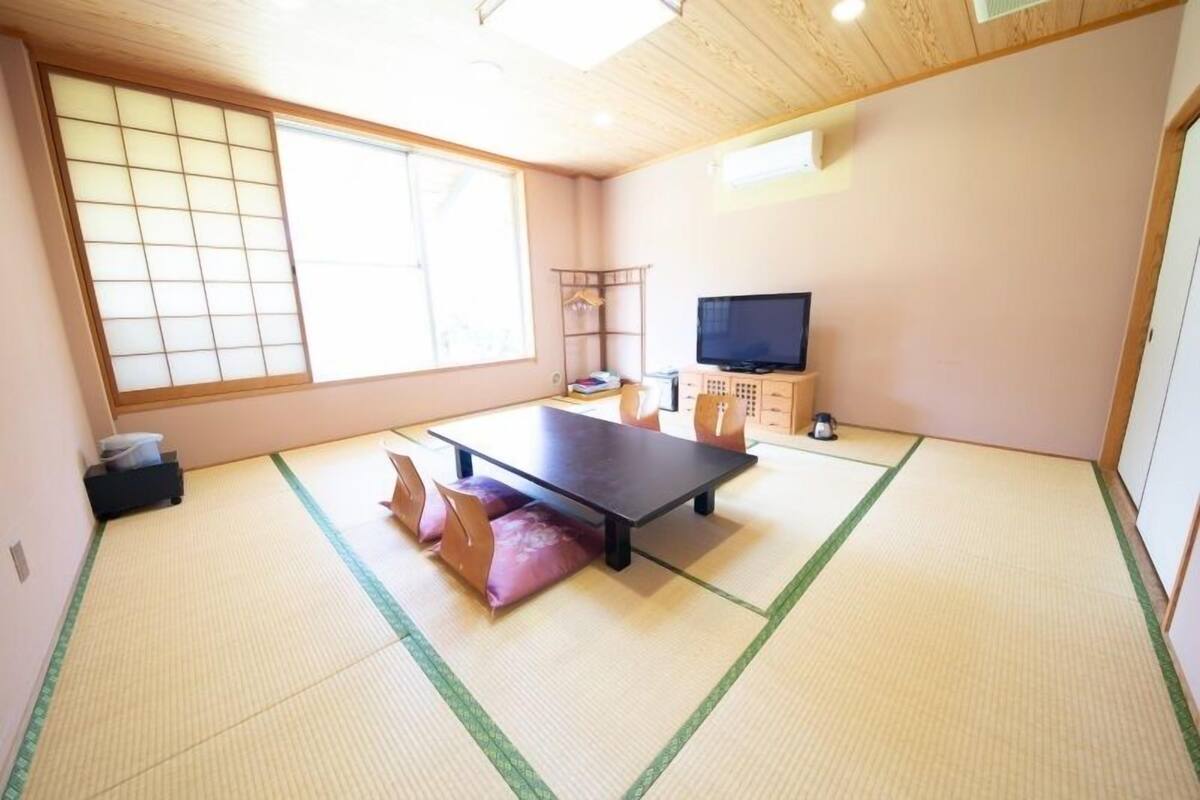 A tatami mat room with a television, a shelf, and a window.