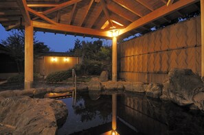Ein ruhiger Außenbereich mit einer Holzpergola, einem kleinen Teich und einer Steinmauer.