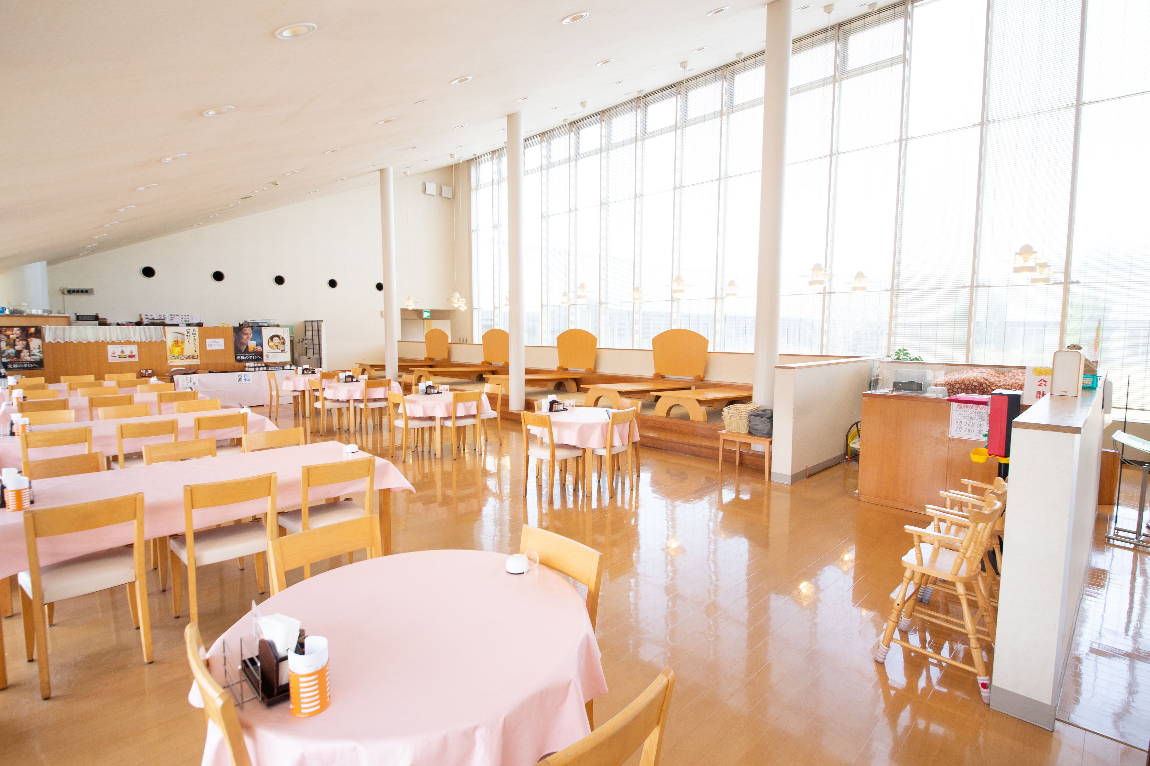 Un vaste espace intérieur aménagé en salle à manger, avec de nombreuses tables et chaises, de grandes fenêtres et un design épuré et moderne.