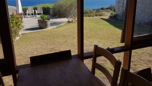 A view from a room with a large window overlooking a grassy yard with a few potted plants and outdoor furniture. - Stone eco-friendly villa, beachfront acreage. Penguins, koalas (Emu Bay)