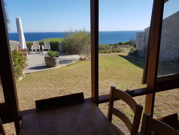 A view from a room with a large window overlooking a grassy yard with a few potted plants and outdoor furniture.