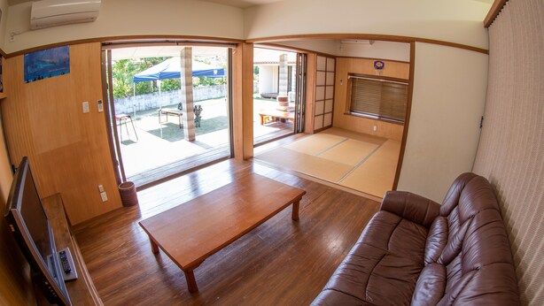 A room with a wooden floor, a brown sofa, a wooden table, and a television. - Minsyuku Meekiya (Nakijin)