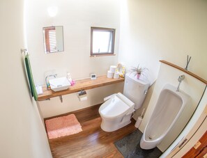 A bathroom with a wooden vanity, a toilet, a bidet, a small window, and a towel rack.