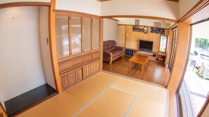 A traditional Japanese-style living room with tatami flooring, a sofa, a television, and a sliding door with a view of the outside. - Minsyuku Meekiya (Nakijin)