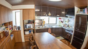 A compact kitchen with wooden cabinets, a central island, and modern appliances including a microwave, oven, and refrigerator. - Minsyuku Meekiya (Nakijin)