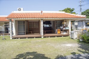 A house with a tiled roof, a porch with a bench, and a small garden area.