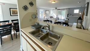 Et moderne køkken med en dobbeltvask, et spiseområde med et træbord og stole, samt et stort spejl der reflekterer rummet.