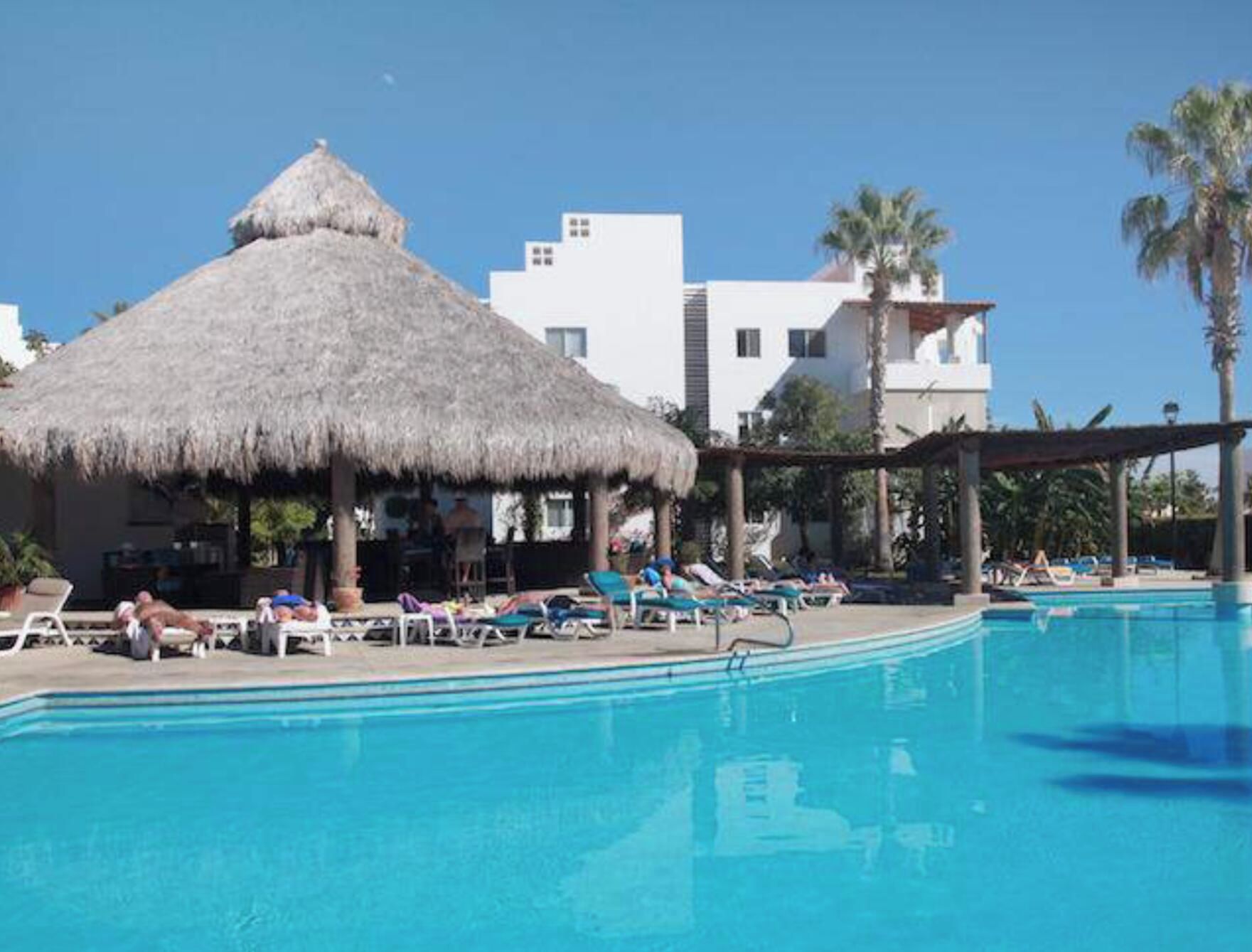 A swimming pool with lounge chairs and a thatched-roof structure.
