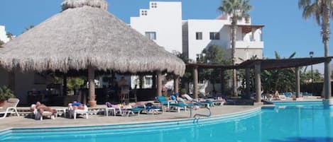 A swimming pool with lounge chairs and a thatched-roof structure.