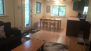 A living room with a sofa, a wooden coffee table, and a dining area with a table and chairs. There is a kitchen area with cabinets and a countertop. - Quaint cabin with Lake Pauline views (Ludlow)