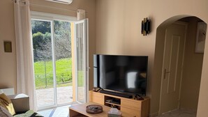 A living room with a sofa, a coffee table, a flat-screen TV, and a sliding glass door leading to a garden.