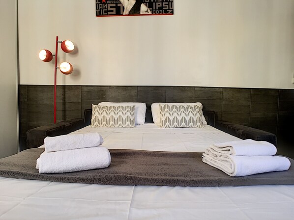 A neatly made bed with two pillows, a dark headboard, and a wall-mounted light fixture.