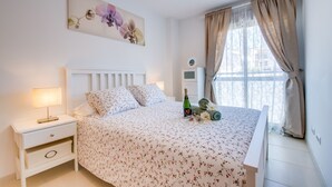 Un dormitorio ordenado con cama, mesita de noche, lámpara y ventana con cortinas.