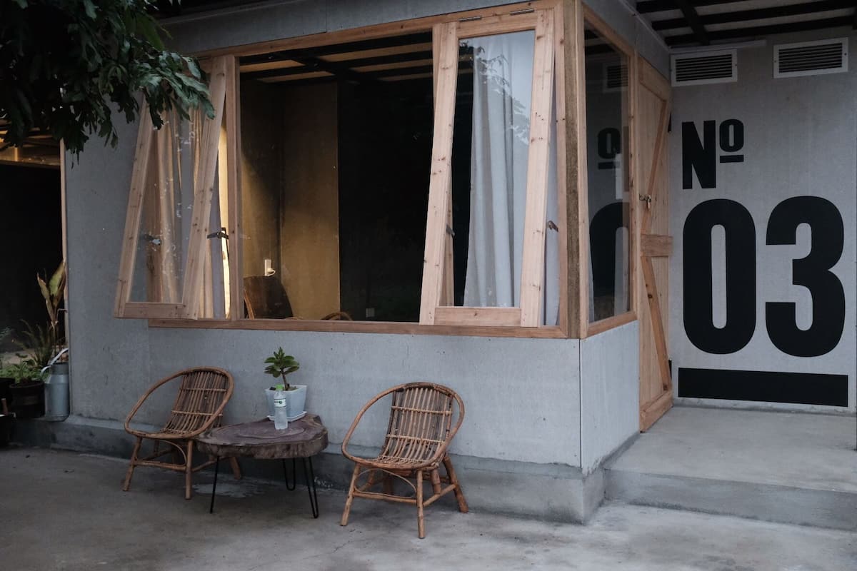 A building with a large window, two wicker chairs, a small table, and a potted plant.