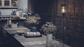 A kitchen with a long counter, two vases with flowers, a marble pitcher, and a floor lamp. - Opal house (Ta Van)