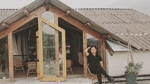 A rustic wooden structure with a large glass door, wicker chairs, and potted plants. - Opal house (Ta Van)