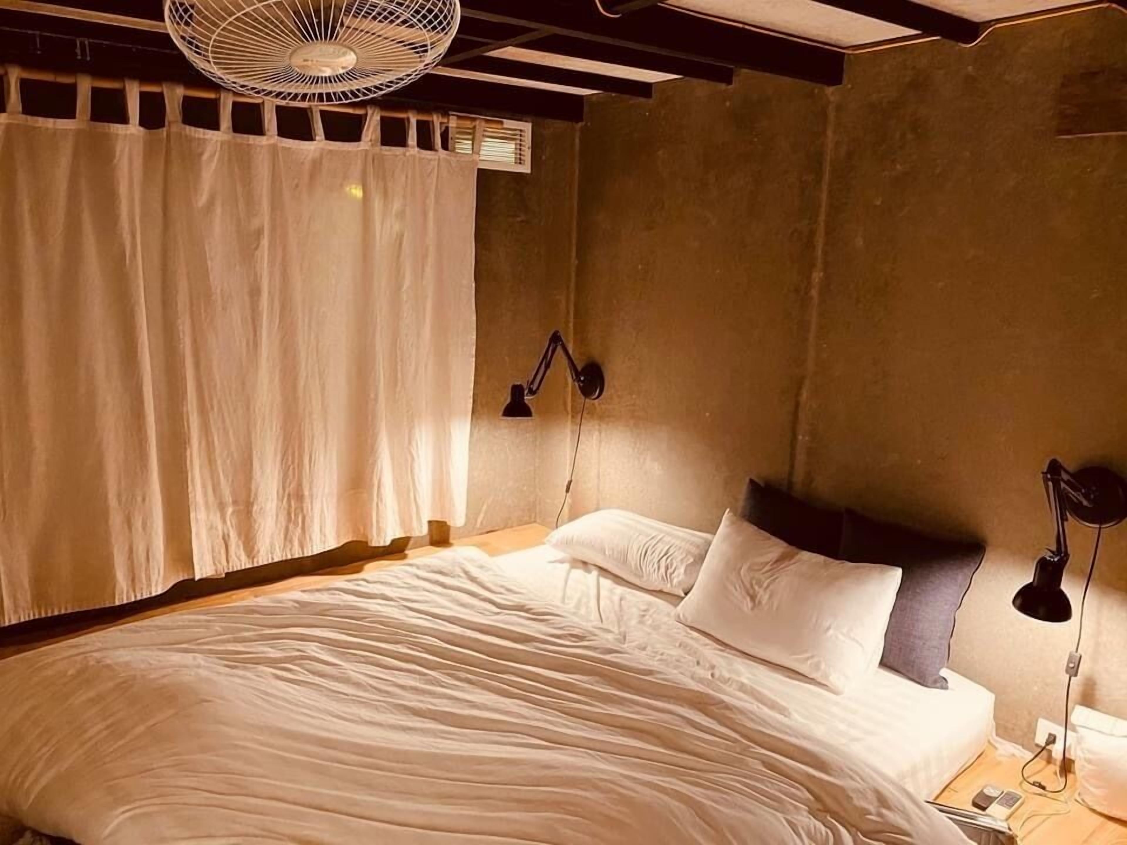 A bedroom with a bed, two bedside lamps, a window with a curtain, and a ceiling fan.