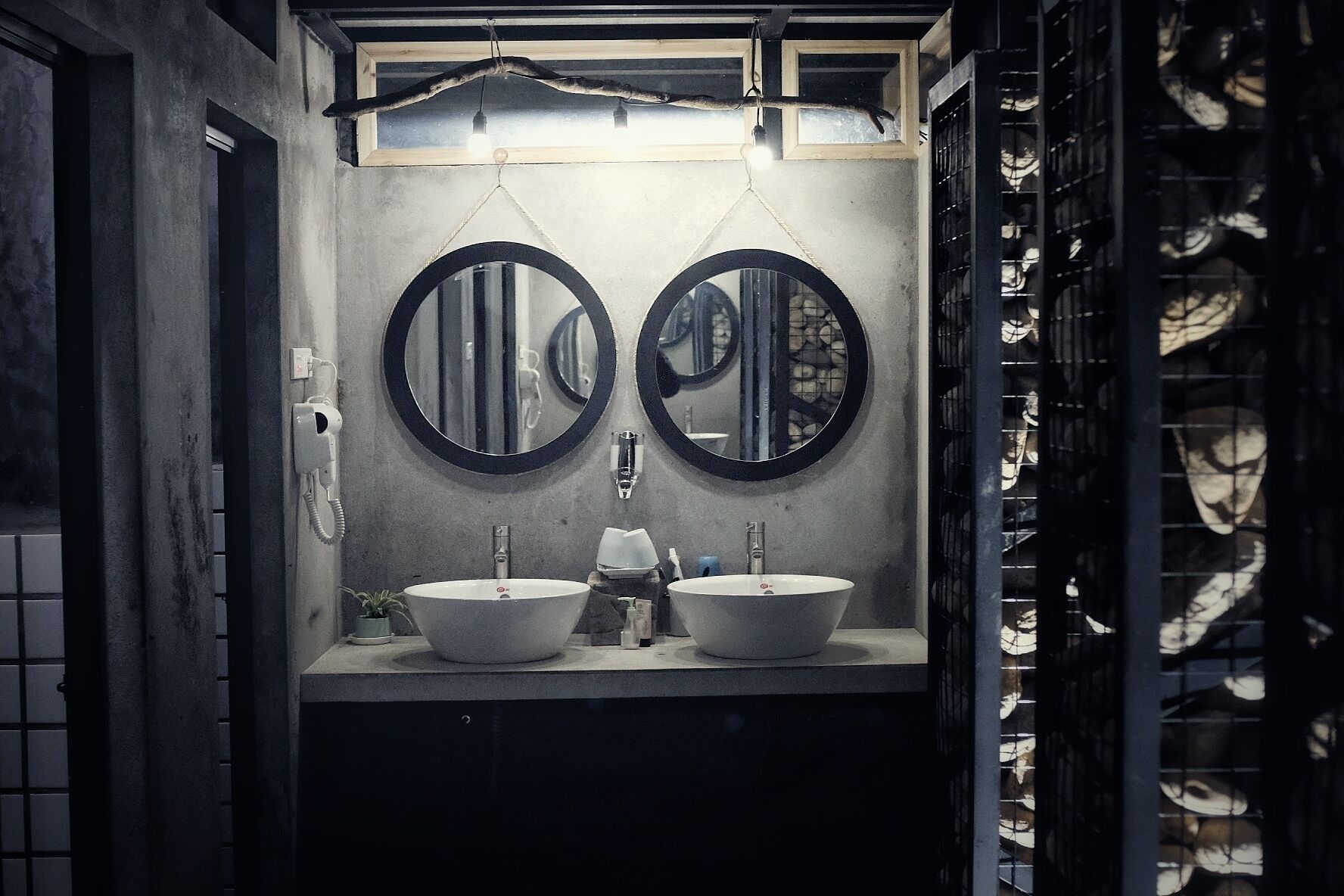A bathroom with two sinks, each with a round mirror above. There is a telephone and a small plant on the counter.