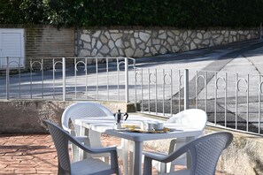 Espace extérieur aménagé avec des chaises et une table blanches, un mur en pierre et une clôture en métal.