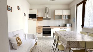 A compact kitchen with a microwave, oven, and a dining area with a table and chairs. - S100 - Sirolo, new three-room apartment with terrace (Sirolo)