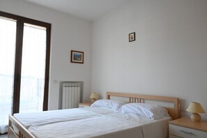 Une chambre à coucher avec un lit, deux tables de chevet, un radiateur et une fenêtre avec des rideaux.