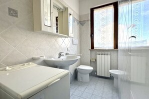 Une salle de bain équipée d’un lave-linge, d’un évier, de toilettes et d’une fenêtre avec des rideaux à motifs.