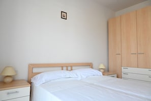 A bedroom with a wooden bed, a nightstand with a lamp, a dresser, and a framed picture on the wall.