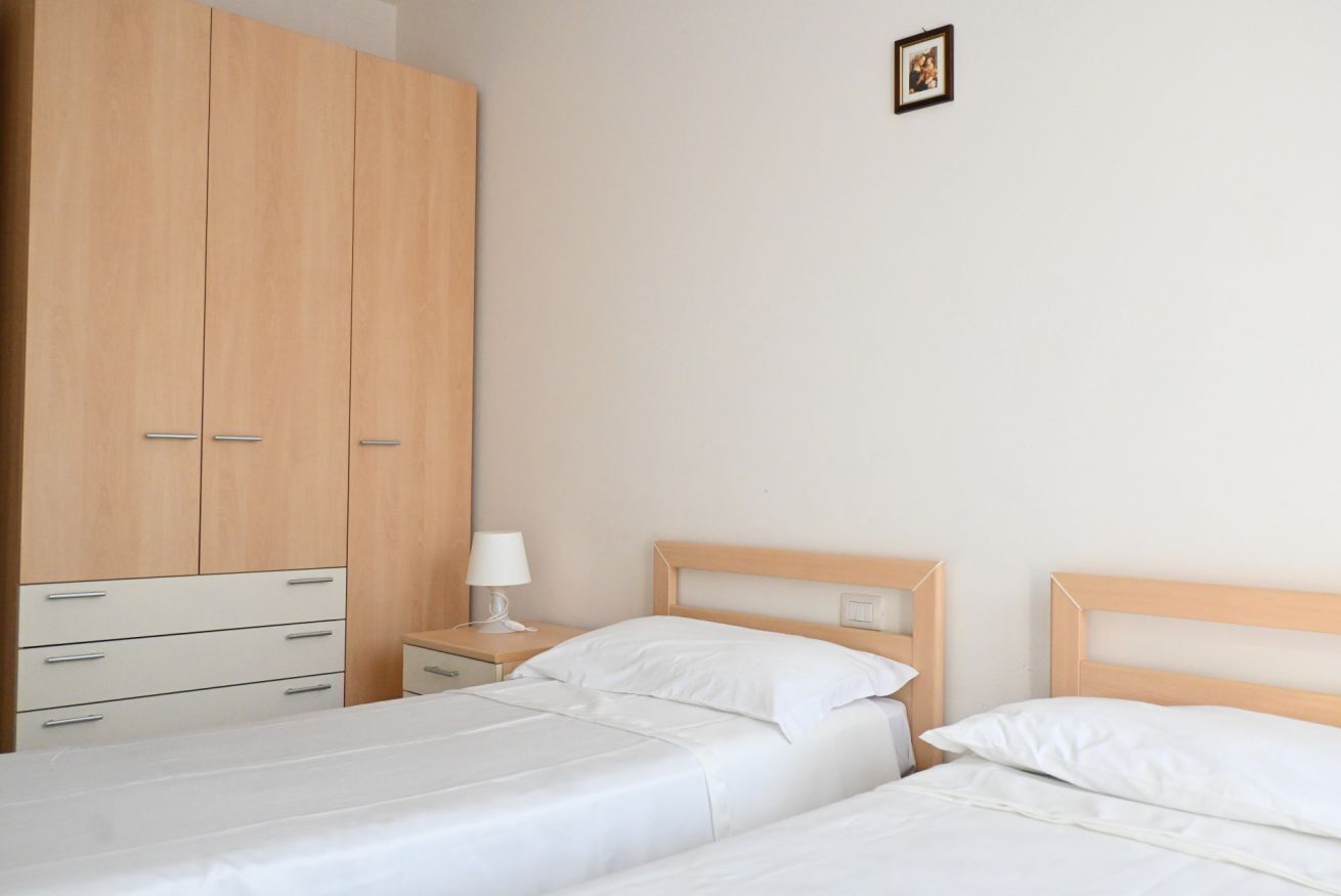 A bedroom with two beds, a wardrobe, a bedside table with a lamp, and a framed picture on the wall.