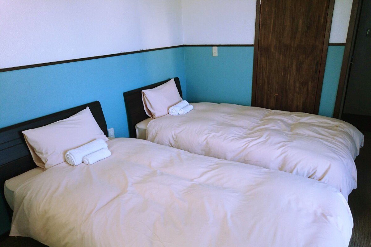 Two single beds with white linens and pillows, a wooden headboard, and a blue wall.