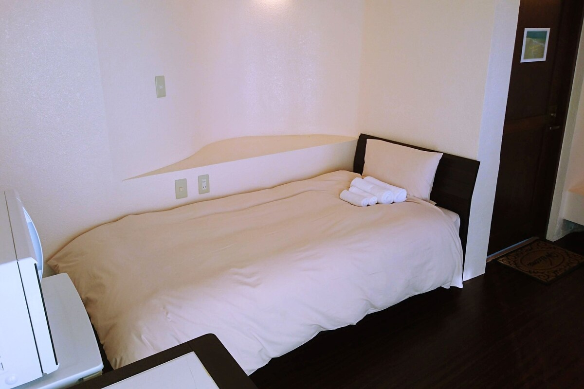 A single bed with a white duvet, a bedside table, and a wall-mounted light fixture.