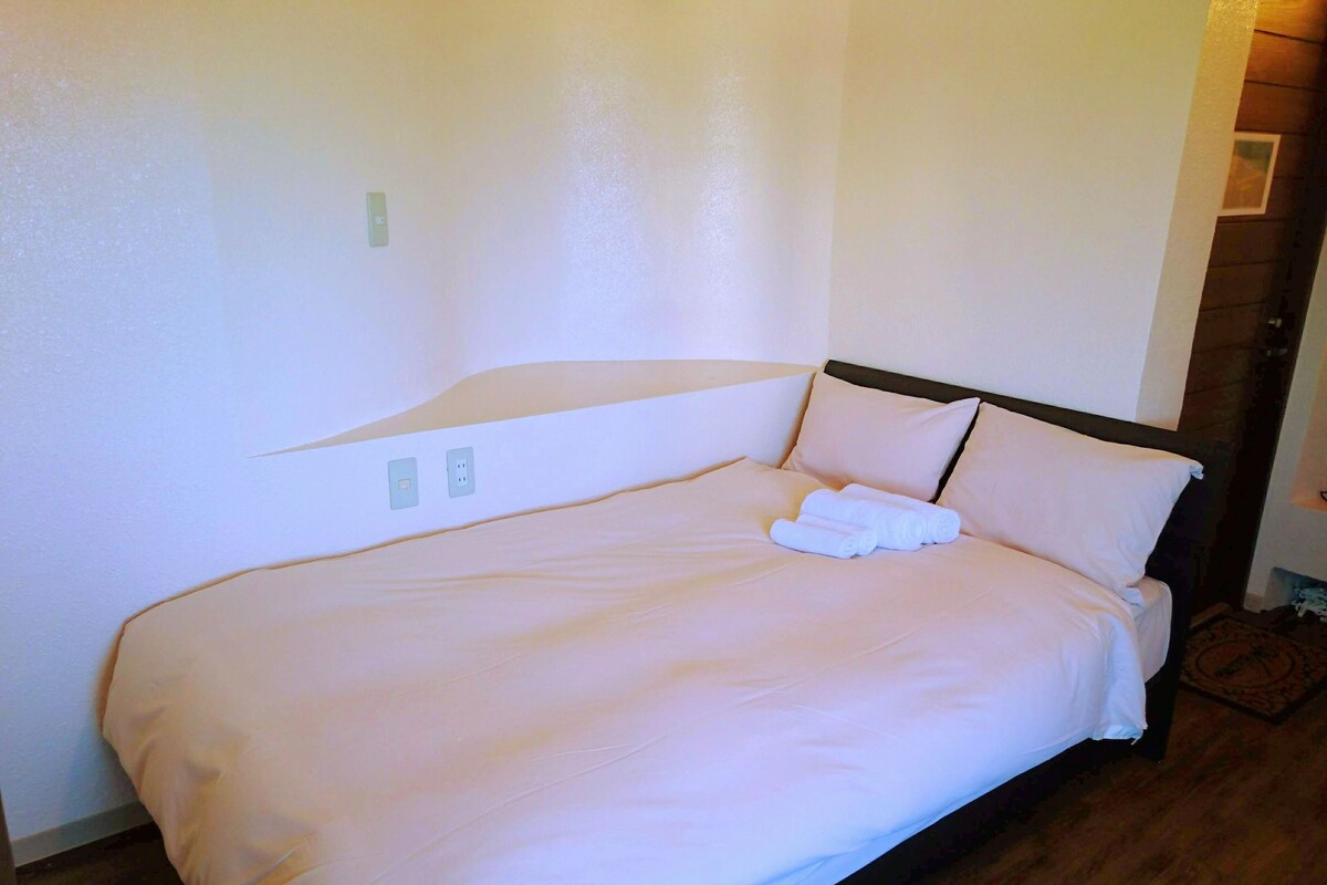 A neatly made bed with a headboard, two bedside lamps, and a power outlet on the wall.