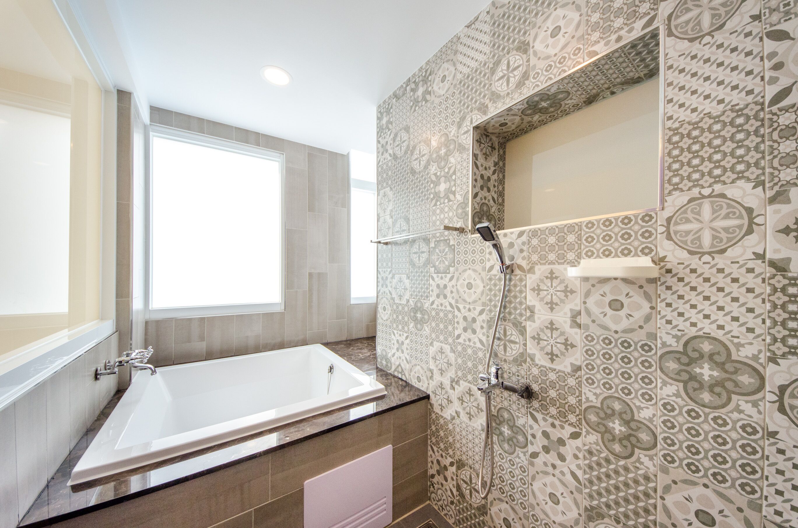 A modern bathroom with a large bathtub, a shower, and patterned tiles.