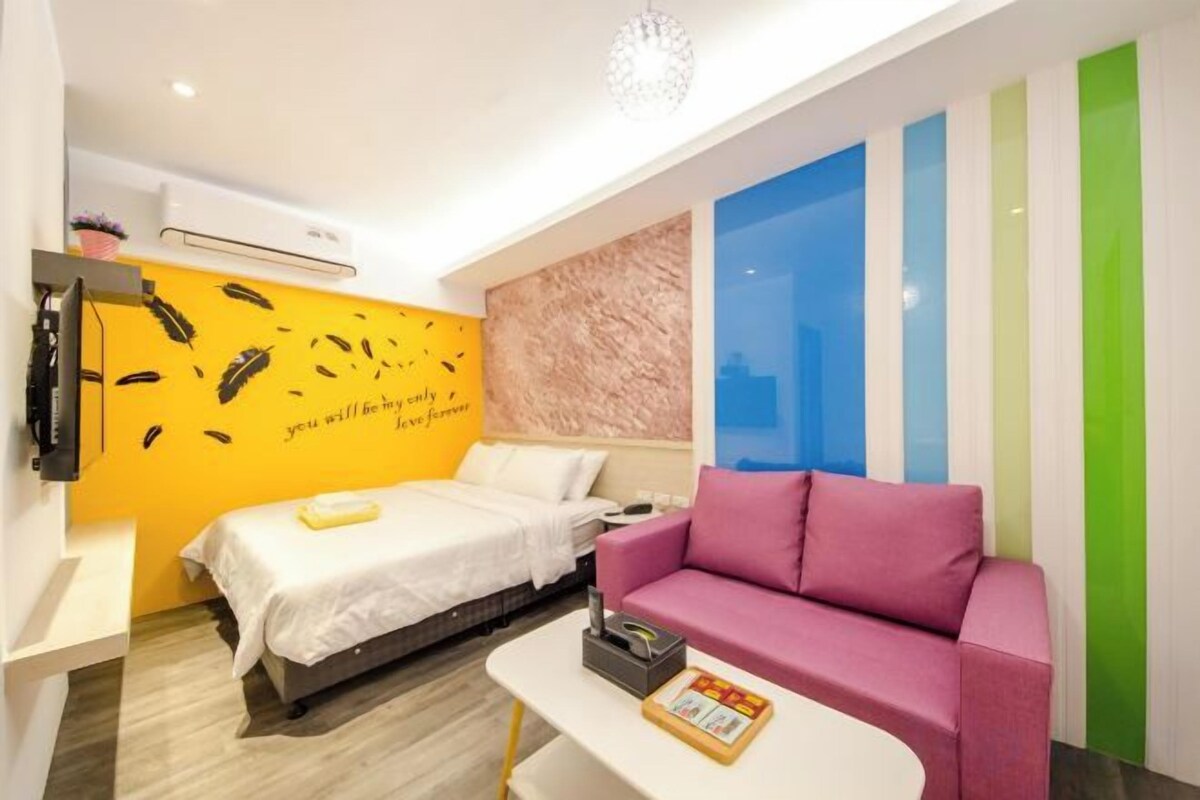 Habitación de hotel con cama, sofá, televisión y pared con rayas verticales.