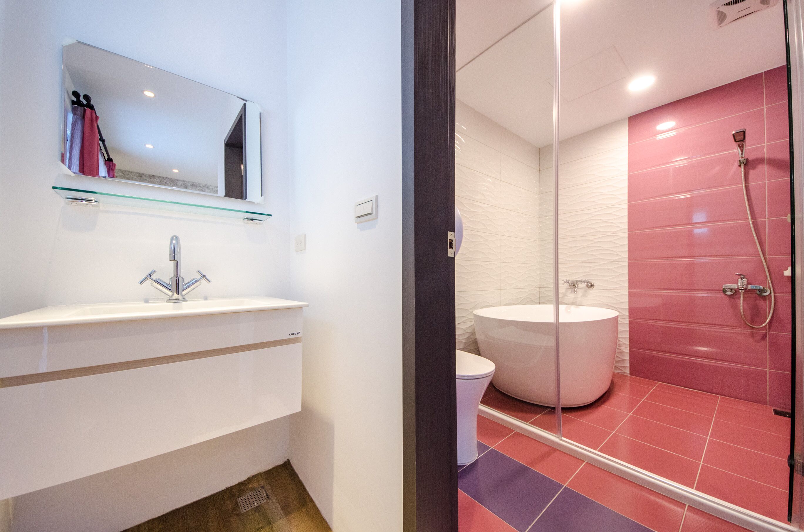 A modern bathroom with a white sink, a large mirror, a glass shelf, a white toilet, and a glass-enclosed shower area with pink tiles.