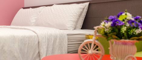 A neatly made bed with white bedding, a small table with a pink toy car and flowers, and a wall with colorful triangular decorations.