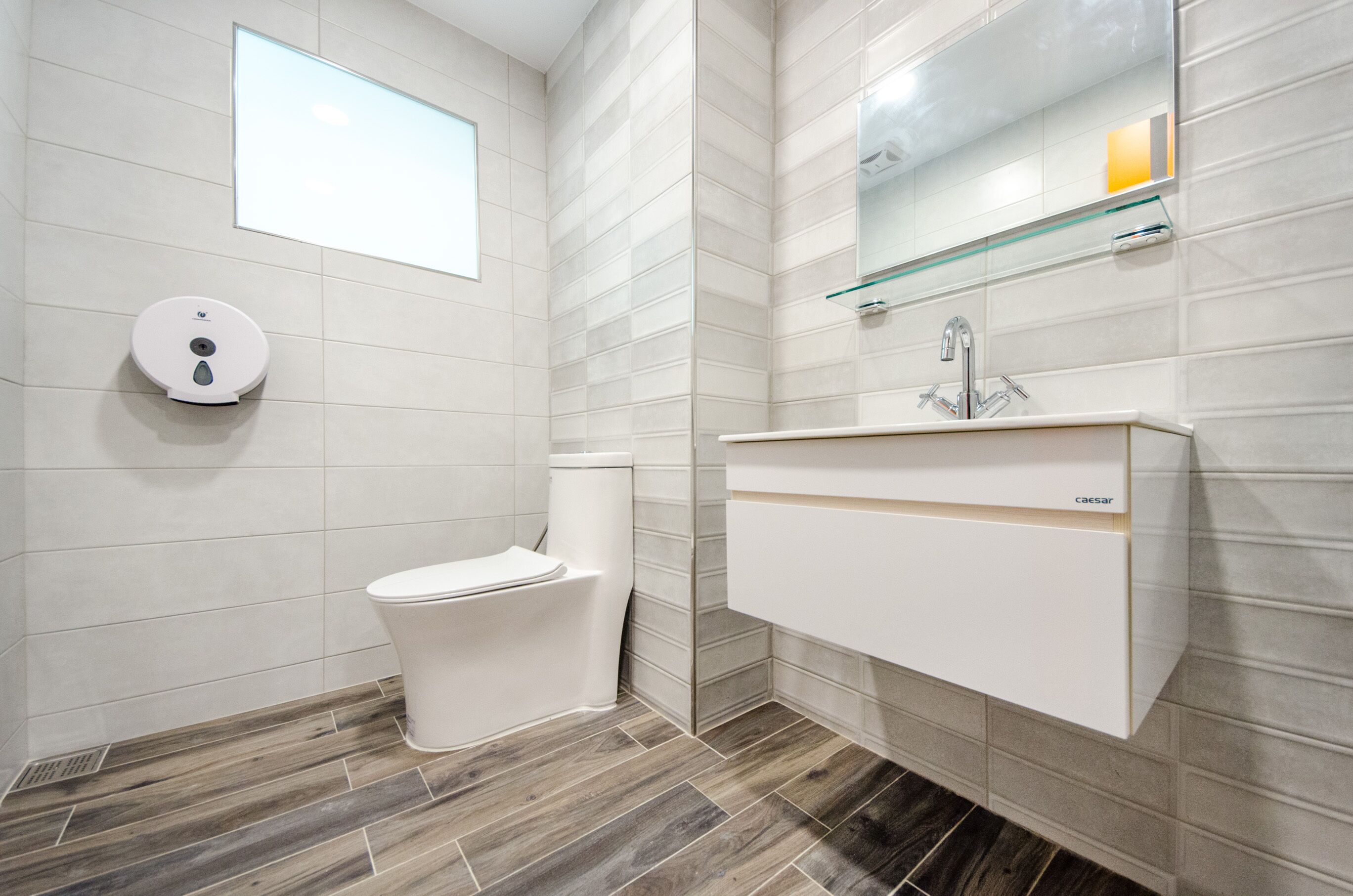 A modern bathroom with a toilet, a glass shelf above the sink, and a wall-mounted mirror.