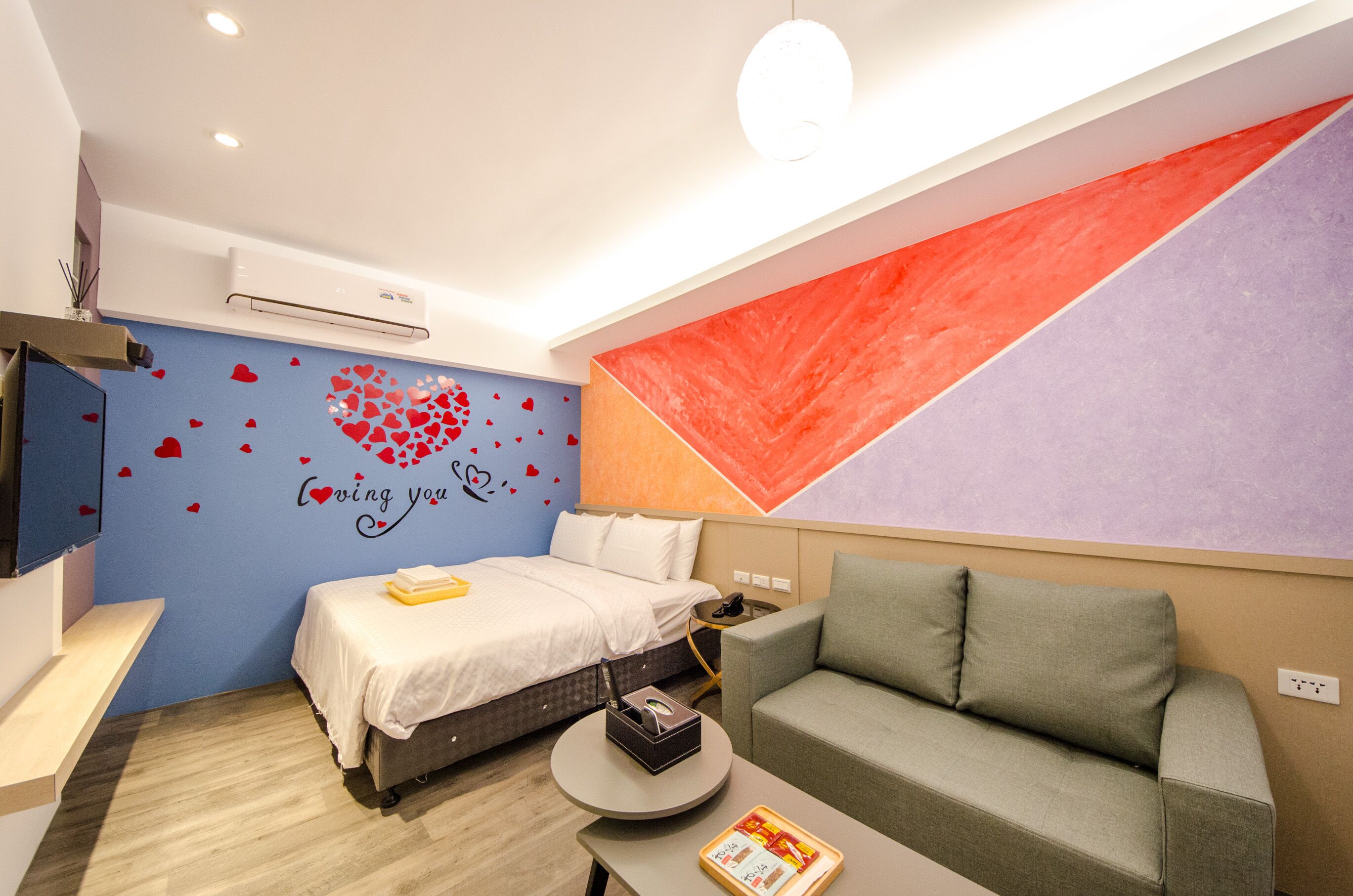 A modern hotel room with a bed, a sofa, a small table, and a wall with a geometric design.