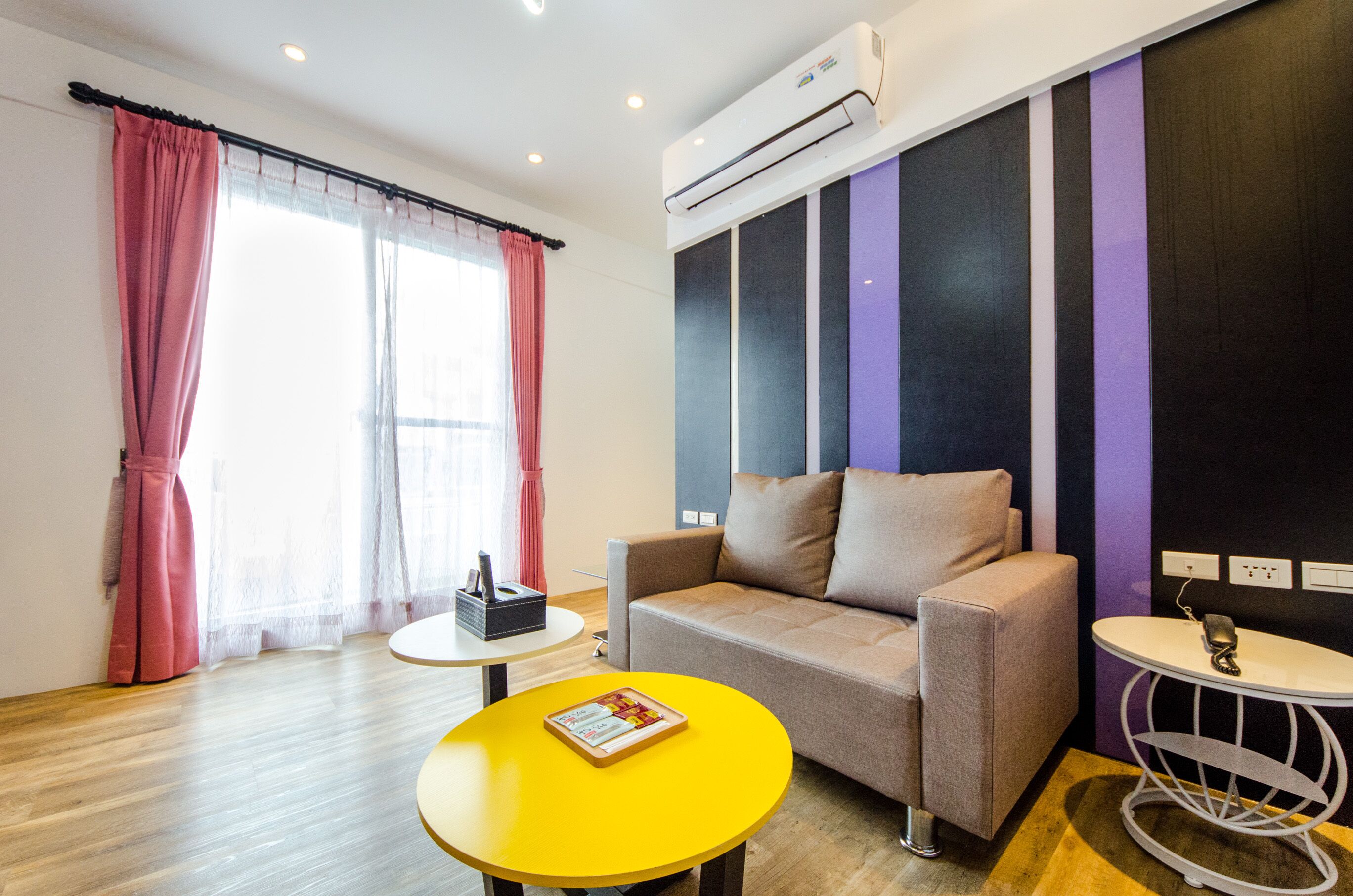A modern room with a sofa, a small table with a book, a decorative table lamp, and an air conditioning unit.