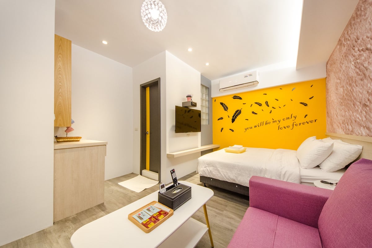 A modern hotel room with a bed, a sofa, a desk, and a wall with a motivational quote.