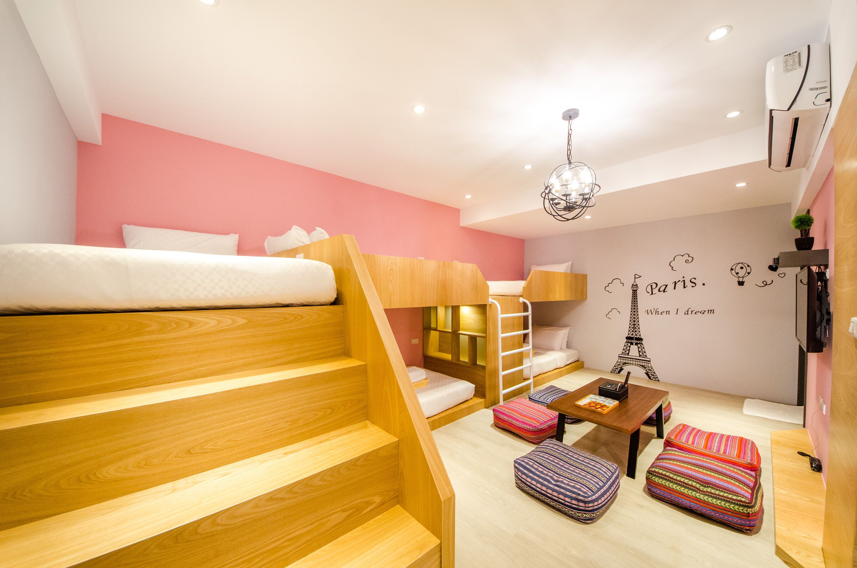A compact room with a bunk bed, a wooden staircase, a small table, and a wall with a Paris-themed mural.