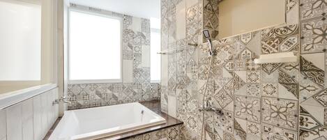 A bathroom with a large bathtub, a shower, and patterned tiles.