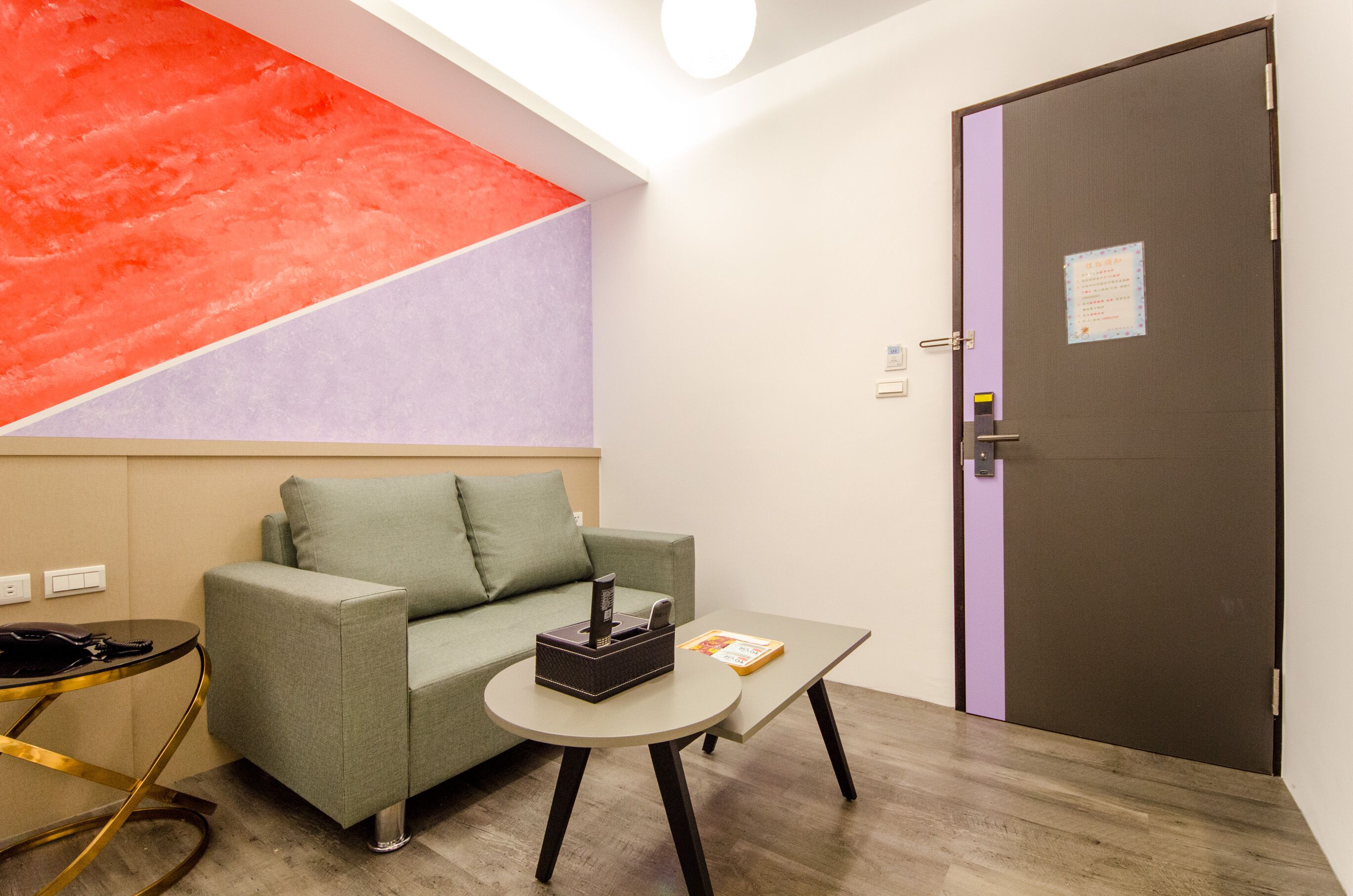 A room with a green sofa, a small round table with a book and a box, a door with a purple stripe, and a red and purple wall.
