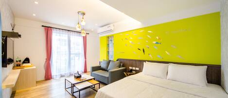 A modern hotel room with a bed, a sofa, a coffee table, and a bright wall with a fish mural.