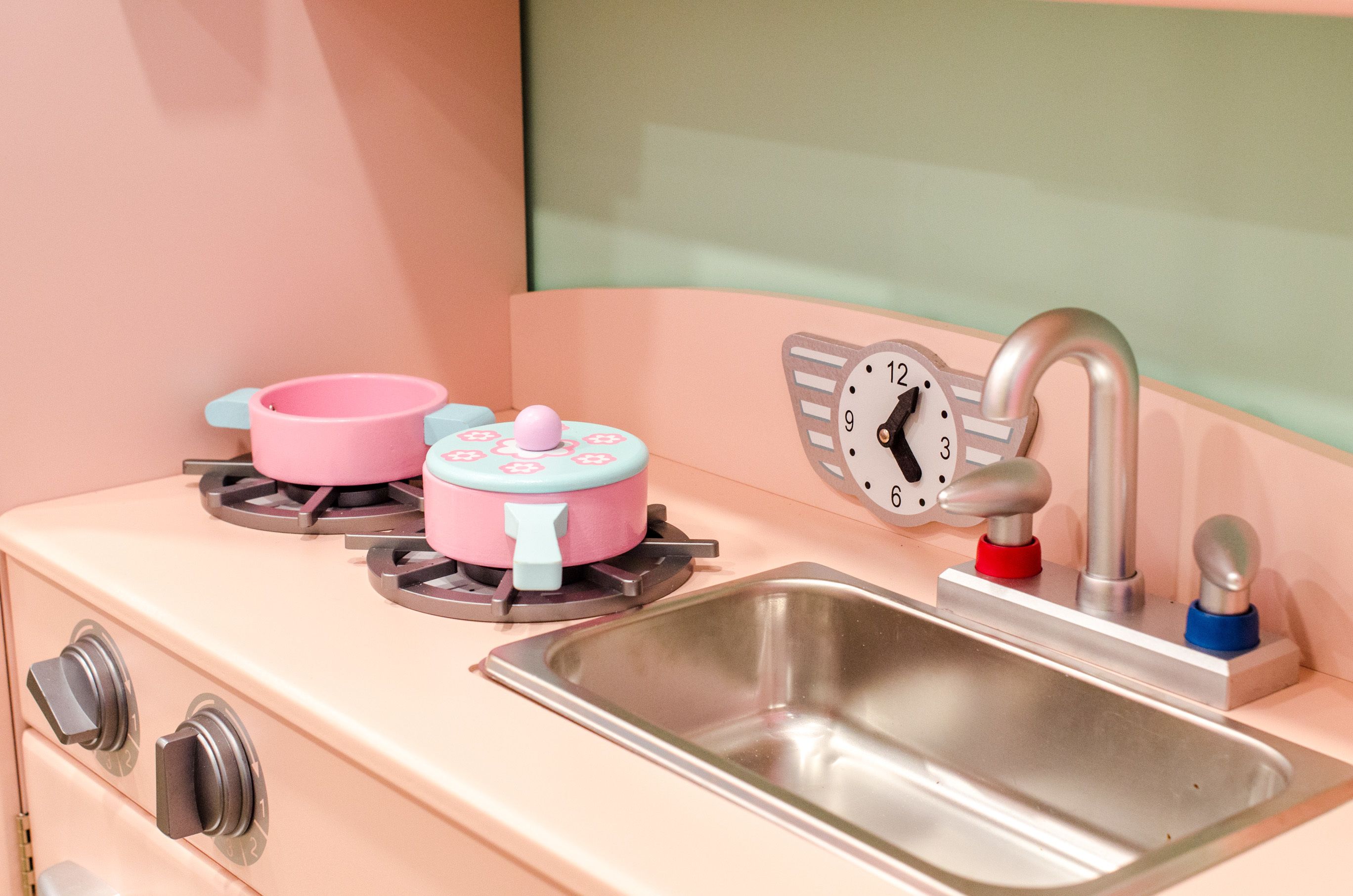 A kitchen with a pink stove, a sink, and a clock.