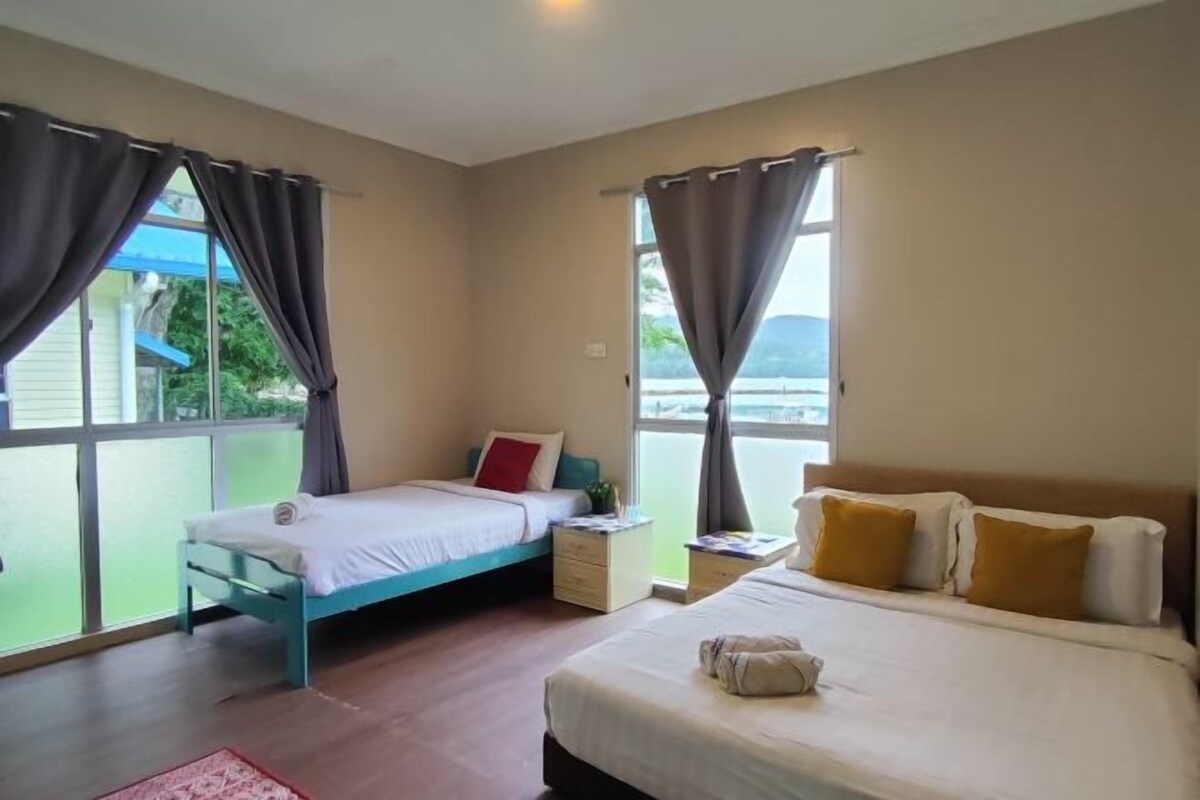 A bedroom with two beds, a window with curtains, a bedside table, and a view of greenery outside.