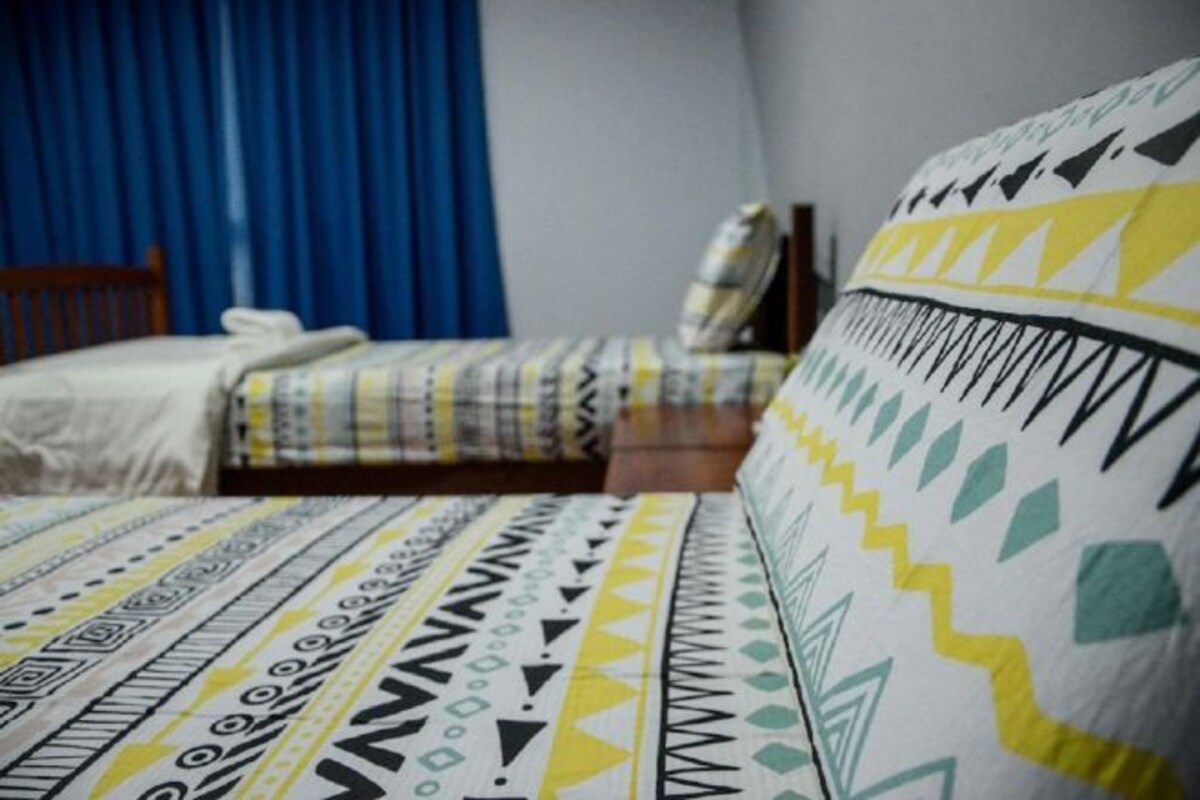 Un dormitorio con una cama cubierta con ropa de cama estampada, un cabecero de madera y una cortina azul.