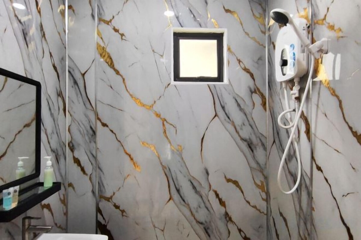 Een badkamer met een marmeren wand, een spiegel, een wastafel en een douche met een handdouche.