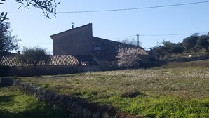 Un muro de piedra, un edificio con techo inclinado y un campo lleno de flores.