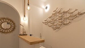 A modern bathroom with a wooden vanity, a round mirror, and a wall-mounted light fixture. - Central suites (Mykonos)